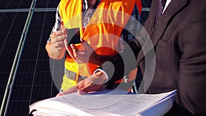 View of an engineer showing photovoltaic detail to client at solar energy station.