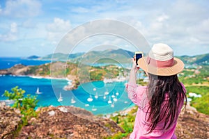 Young tourist woman making photo of English Harbor from Shirley Heights, Antigua, paradise bay at tropical island in the photo