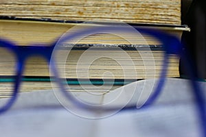 View through enlarging zoom lens of blue reading glasses on pile of antique yellowed books