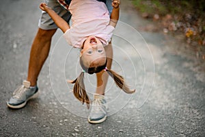 View on face of happy girl in pink t-shirt which her father hold upside down and swing her