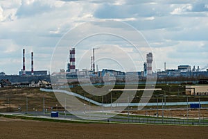 View of a factory with pipes next to an agricultural field. An oil refinery near the city against the background of clouds