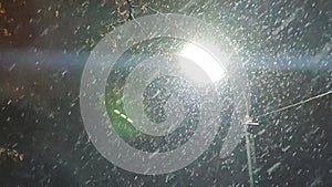 View of falling snow against backdrop of light of glowing lantern at night.