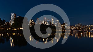 View of False Creek bay in the dark in Vancouver, Canada with the lights of illuminated buildings reflected in water.