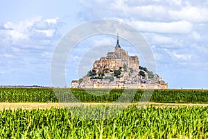 View of famous historic Le Mont Saint-Michel tidal island with green corn fields infront