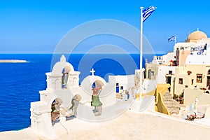 View of famous Oia village with typical church tower and Greek flag, Santorini island, Greece