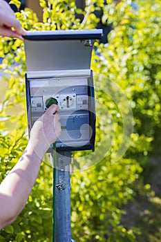 View of female hand connecting cable to outdoor power outlet. Technology concept