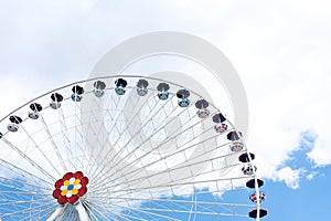 View of the ferris wheel against the background of blue sky and white clouds. Entertainment concept