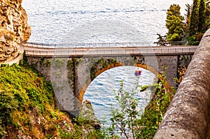 View on Fiordo di Furore arc bridge built between high rocky cliffs above the Tyrrhenian sea bay in Campania region. Boat floating