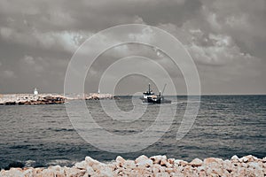 View of a fishing boat returning from the sea to land at sunset and a view of the small harbor,