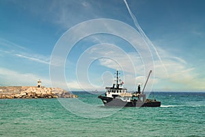 View of a fishing boat returning from the sea to land at sunset and a view of the small harbor,