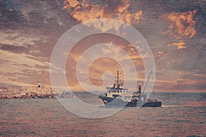 View of a fishing boat returning from the sea to land at sunset and a view of the small harbor,