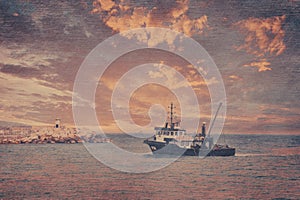 View of a fishing boat returning from the sea to land at sunset and a view of the small harbor, lighthouse