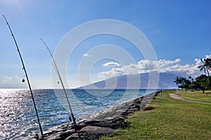 View of fishing rod anchored between rocks,  Hawaiian ocean, and an island seen from a park in Maui