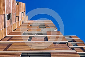 View from the floor of the facade of a modern building clad in ecological wood over clean blue sky, concept of sustainable
