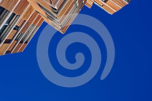 View from the floor of the facade of a modern building clad in ecological wood over clean blue sky, concept of sustainable