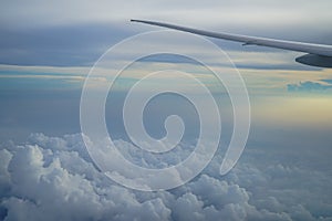 View of fluffy abstract white cloud and blue sky with airplane wing and sunrise light background from airplane window