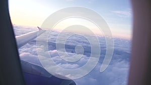 View from flying airplane window wing and white clouds while morning sunrise. Aerial landscape sunset in cloudy sky from