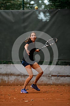 view of focused female tennis player with racket ready to hit a tennis ball.