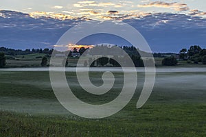 View of foggy green fields and meadows at sunset