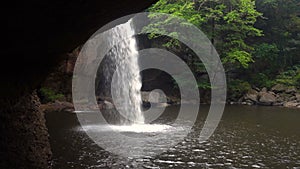 View form Cave under the Picturesque Waterfall in Jungles at Evening Time. Water is Falls in Pool through Sun Beams at