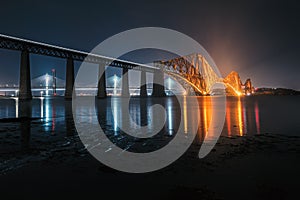 View of Forth Rail Bridge at night and and the glow trail of a moving train over the sea