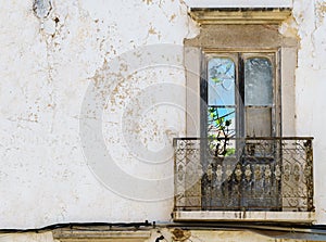 The view through the french window in a dreary weathered house facade in Portugal reveals the vibrant beauty of nature.