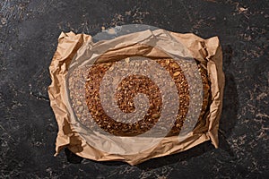 View of fresh baked loaf of whole grain bread in paper on stone black surface