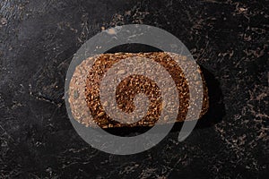 View of fresh baked loaf of whole grain bread on stone black surface