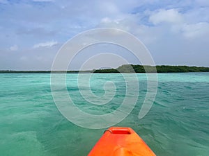 View from the front of a bright orange kayak paddling across a turquoise Caribbean Sea under a blue sky off the island of Bonaire