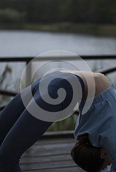 View on a girl with athletic body in blue gym suit is doing gymnastic exercises in the park