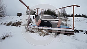 View of girl in balck dress lying on ground covered with snow. Brunette wears VR glasses and pretends that it`s summer