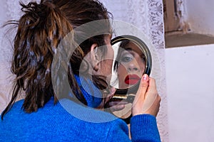 View of girl painting her lips and looking in the mirror at home.