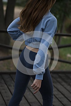 View of a girl's athletic body in blue gym suit in the park in cloudy weather