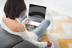 View of girl studying online with laptop and writing in notebook at home