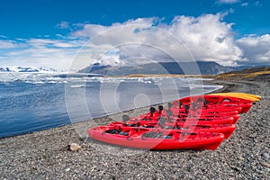 View of Glacier Lagoon with icebergs and red canoes in row, Jokulsarlon, Iceland, summer time