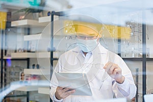 View through glass asian man professional optician selling wear protective face mask selective of glasses in optical shop.