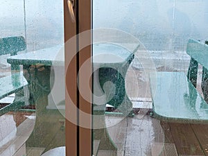 view through a glass door wet from rain to an open terrace with wet furniture
