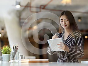 View through glass wall of female office worker writing on schedule book