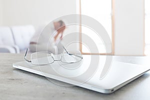 View of glasses lying on the modern laptop with hard thinking man sitting on sofa on the background