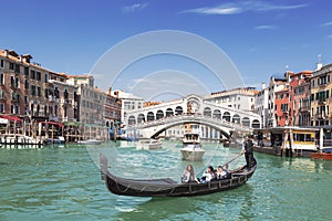View of the Grand Canal, gondola with tourists and the Rialto Bridge. Venice
