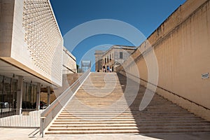 View of the grand stone staircase in the old town of Valetta, Malta. Part of the parliament building on the side. The sky is blue