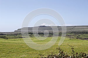View of grass and rocky landscape in western Ireland with ancient fort in background