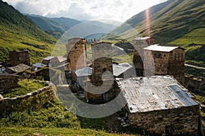 view of grassy field with old weathered rural buildings and hills on background, Ushguli,