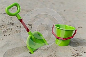 View of a green bucket and scoop at the beach with sand in the background