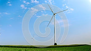 View on green fields and meadows with working wind powered turbines generating electric power