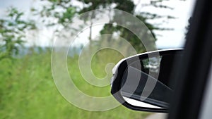 view of green forest from car side mirror. close up of car side mirror while driving. travel and trip concept.