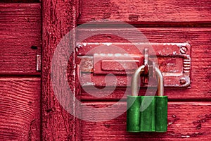 View of green old padlock on the red wooden door.