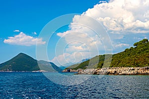 View of green wooded mountains and blue sea, blue sky and white clouds.