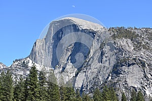 View of Half Dome massive granite wall with a daytime moon above in Yosemite Valley, California