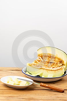 View of half green melon in white plate on wooden table, with pieces of melon and knife, selective focus